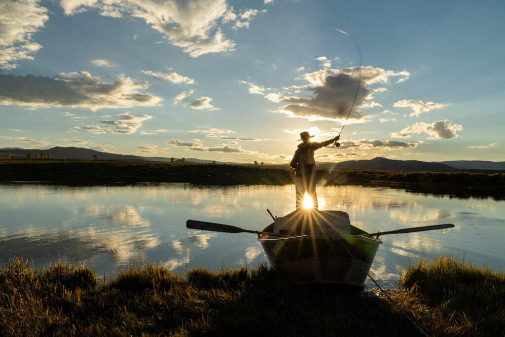 Person stands on row boar casting while the sunset shines behind her