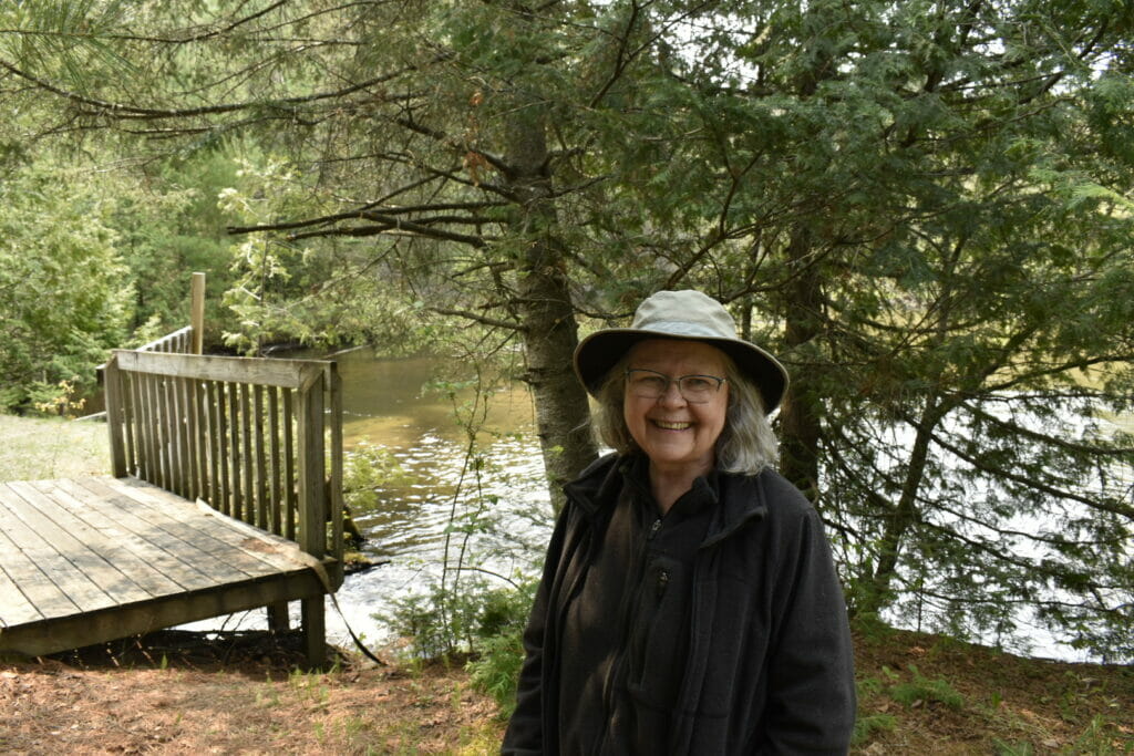 Woman in a bucket hat smiles at the camera in front of a river