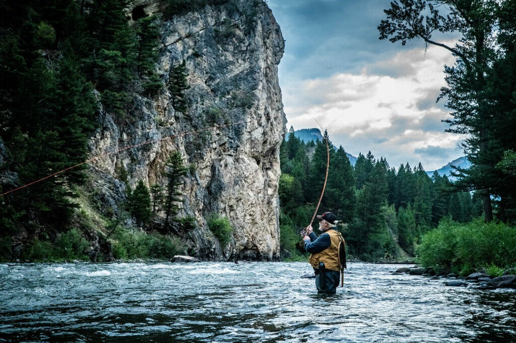 Wide shot of an actor casting a fly fishing line in a mountainous river