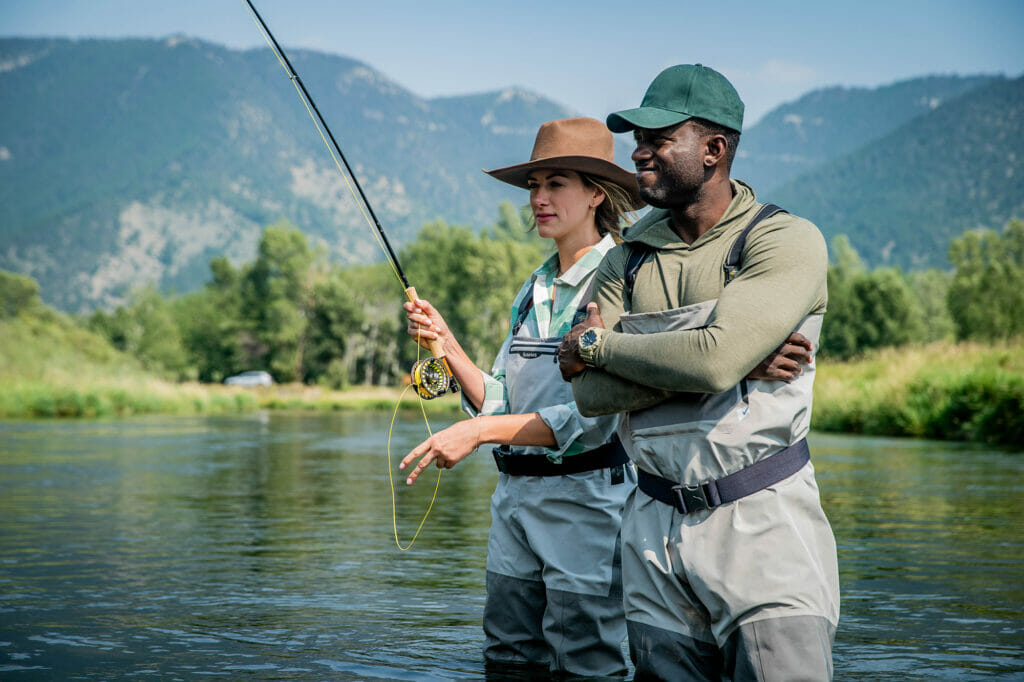 A man and a woman stand in a river while fishing