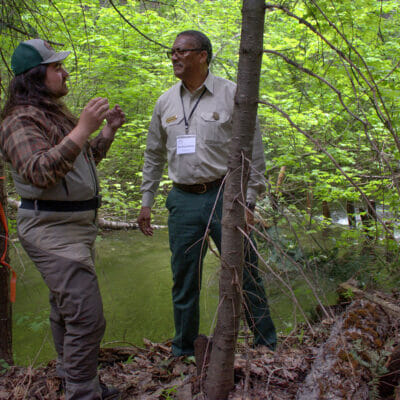 Two men have conversation next to a stream
