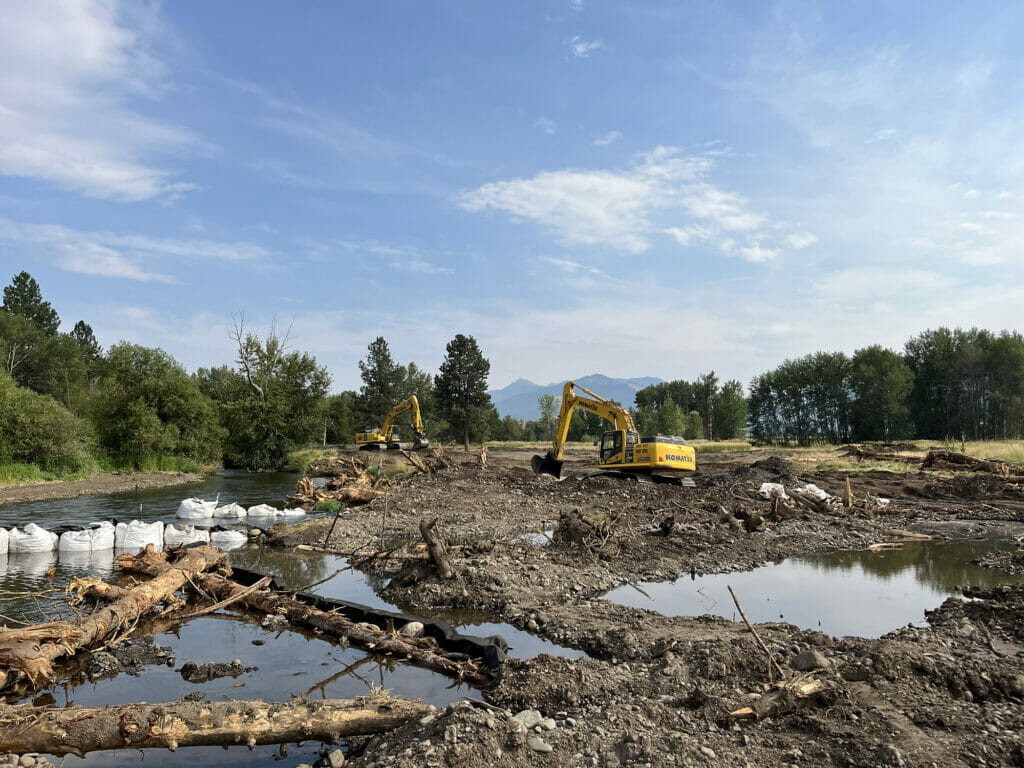 Two backhoes surrounded by up-turned dirt next to a stream