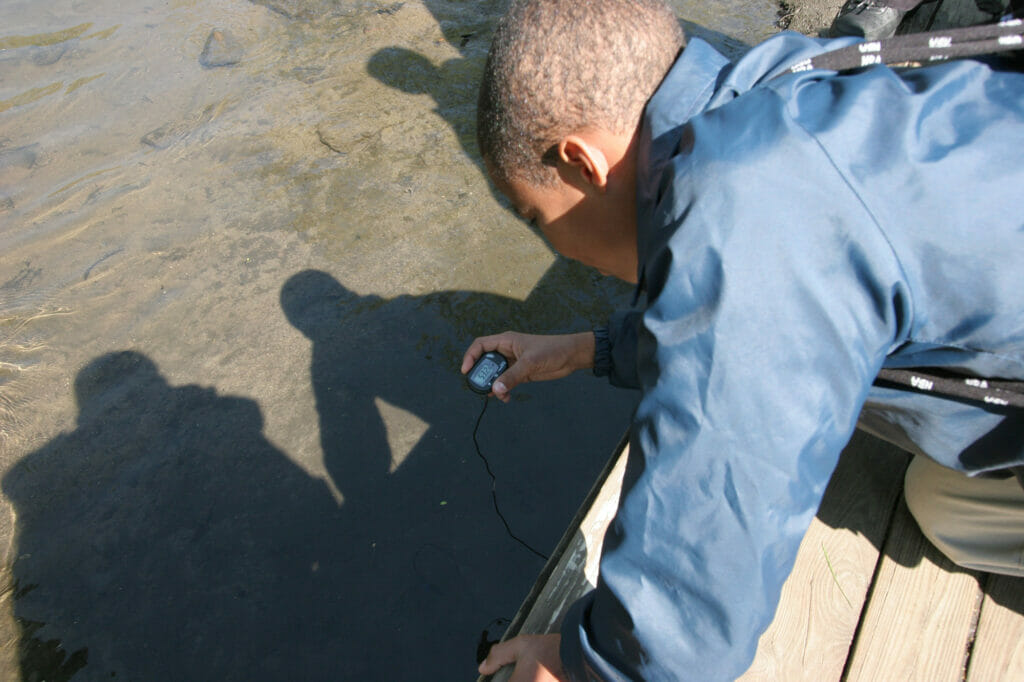 A young student leans over a dock to take the water's temperature