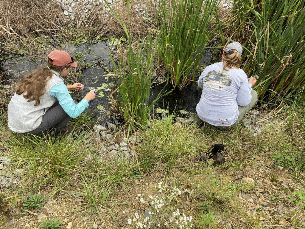 Two women crouched down taking water samples hope for abandoned mine drainage
