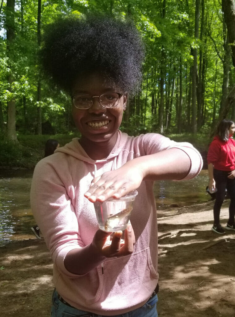 A smiling student holds a jar containing a small fish