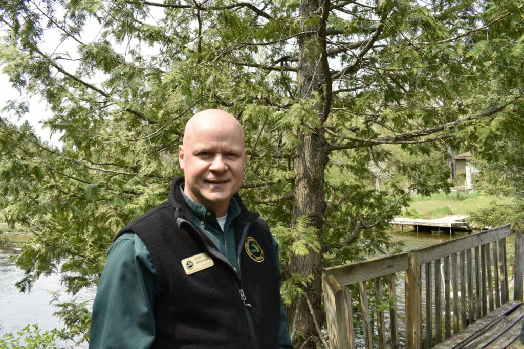 Man in a fleece jacket and name badge looks at the camera in front of a river