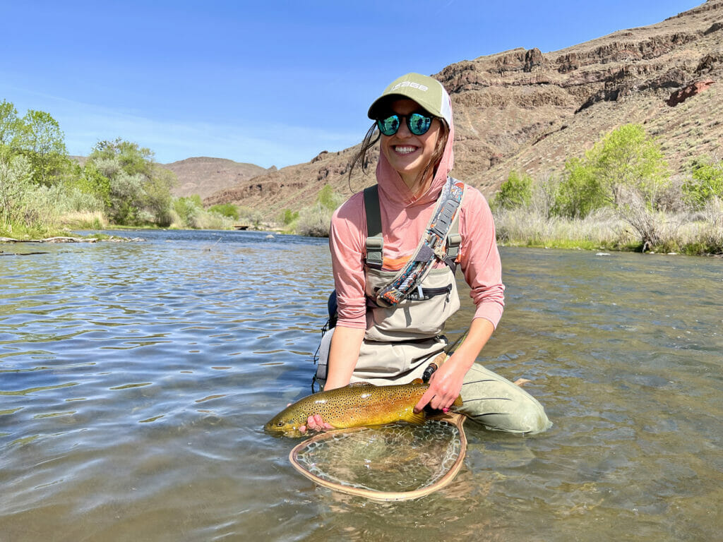 Smiling woman crouches in a stream with a trout in Owyhee Canyonlands