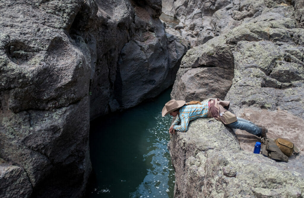 Woman leans over rock, looking into river hoping to be successful