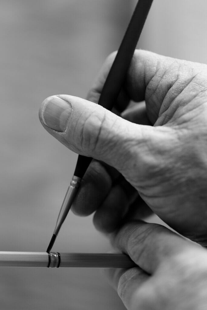 Black and white photo of man painting stripes on a bamboo rod