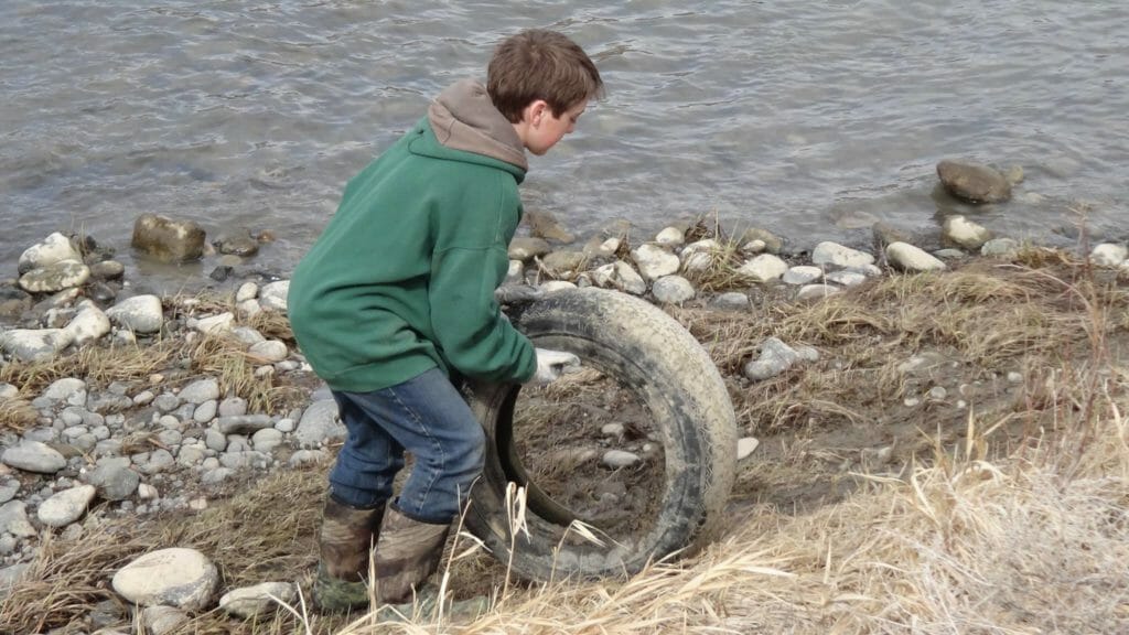 11 year old boy removes an old tire from a river