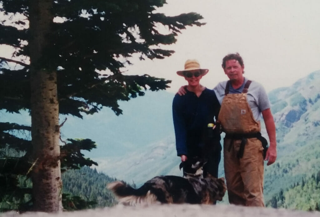 Man stands with an arm around a woman in front of mountains