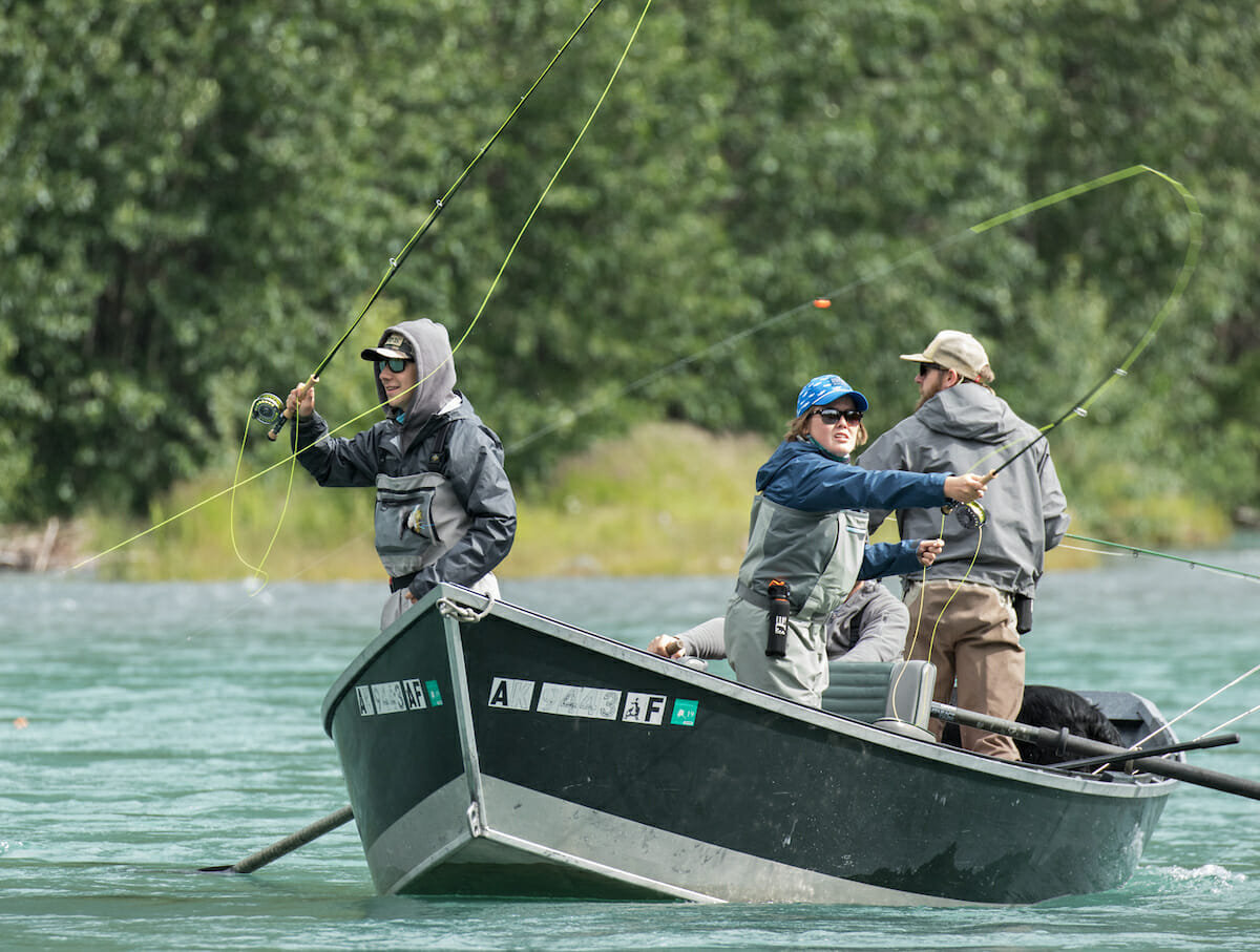 Three people stand in a boat coasting in a chilly day