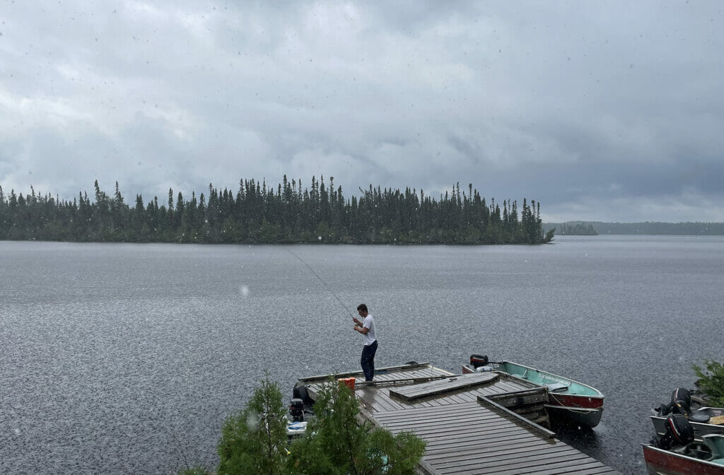 Young man on fishing from a dock while it rains