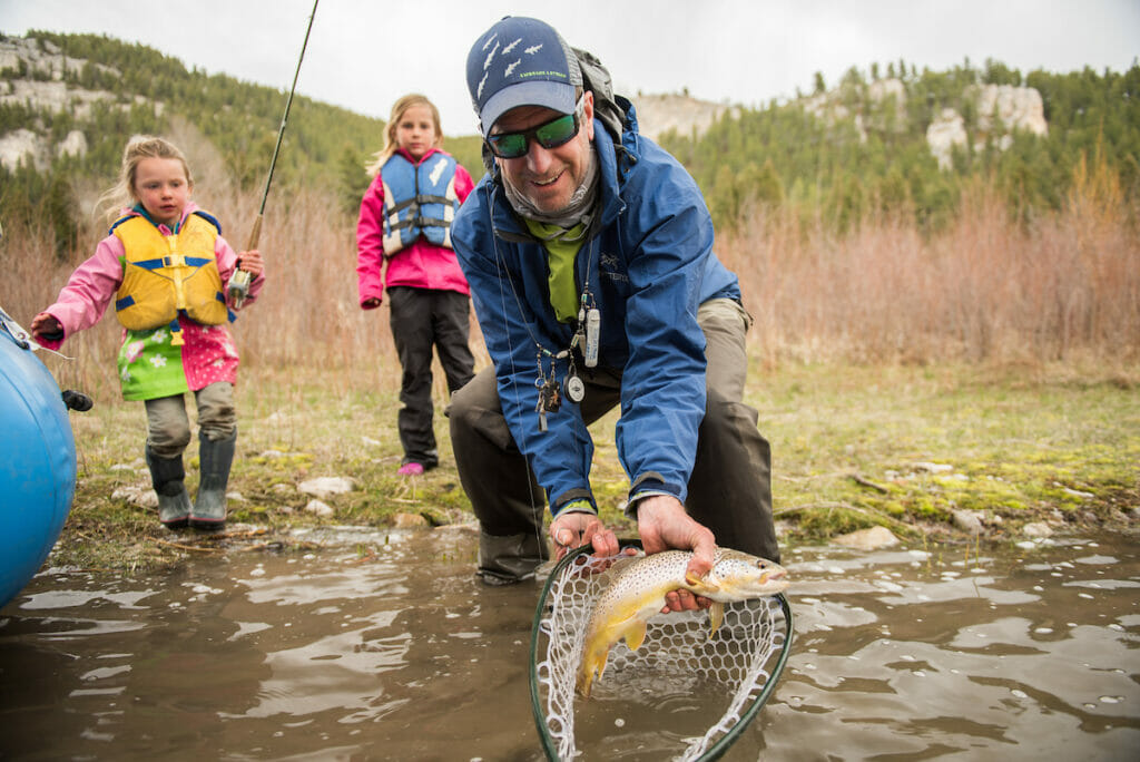 Man catches fish in a net while two kids watch