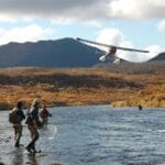 A sea plane about to land on a river by some fishing people