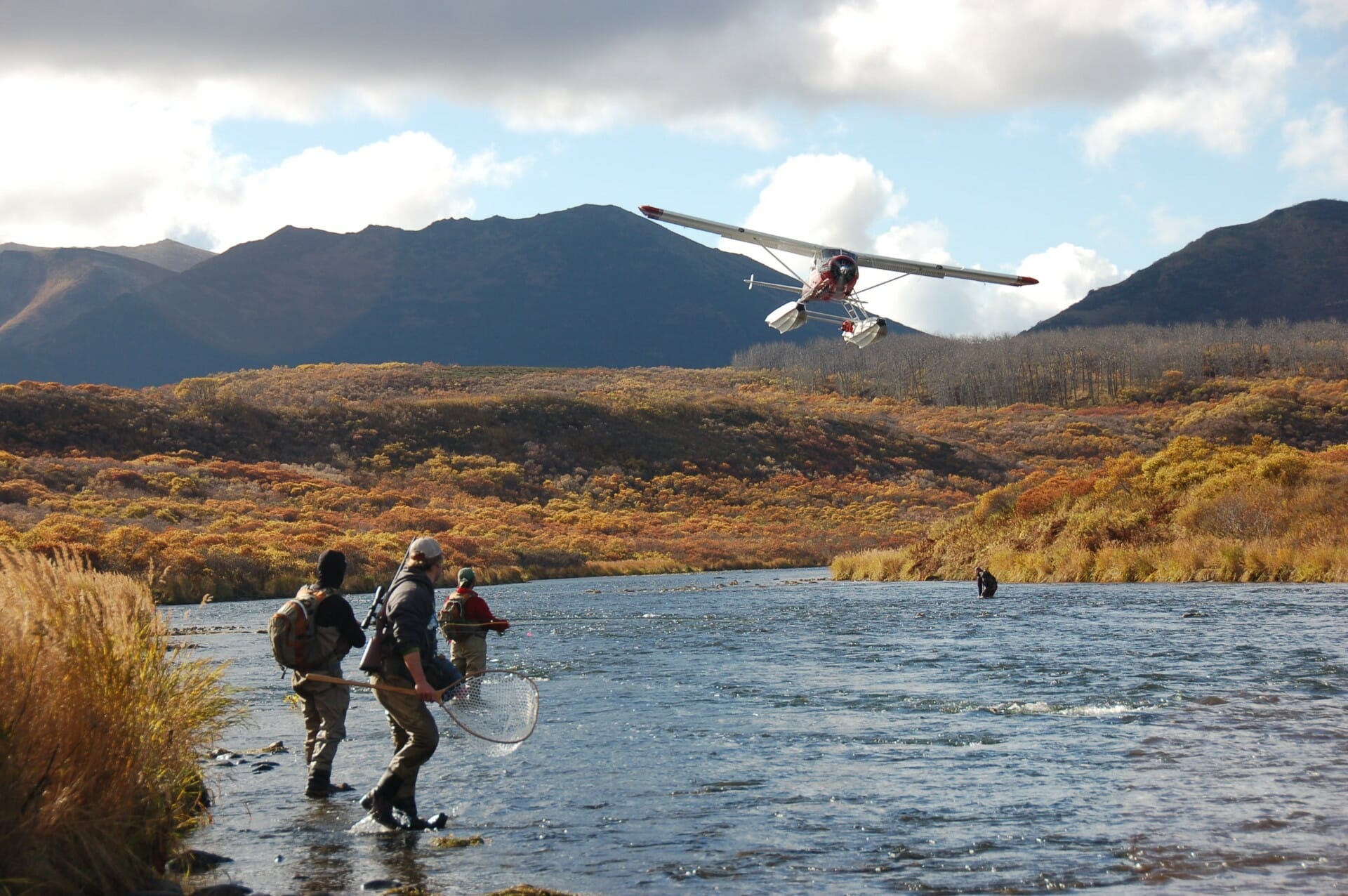 A sea plane about to land on a river by some fishing people