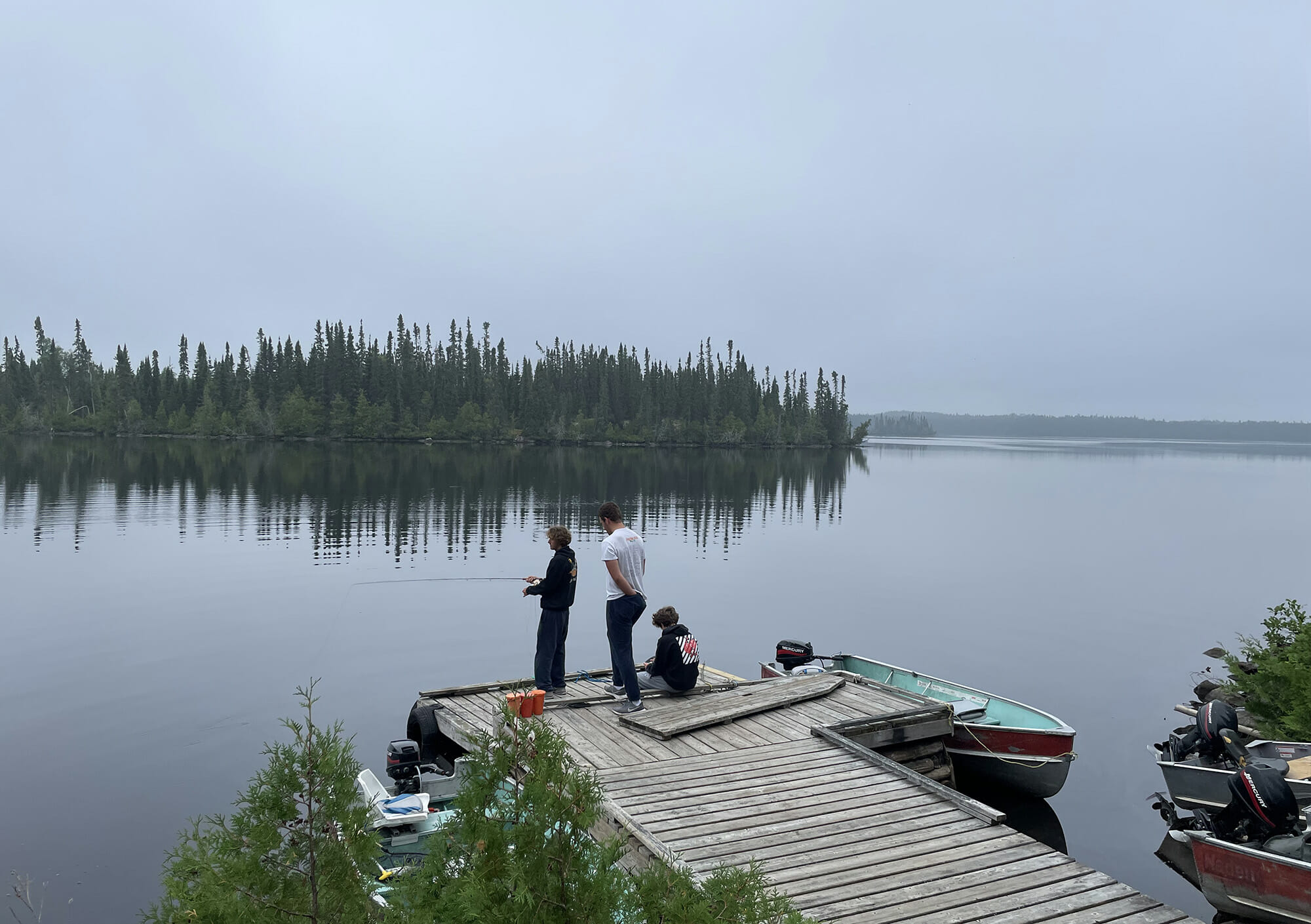 Three young men fishing from a dock with a big, beautiful, calm lake in the background