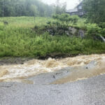 Rain water floods the side of a road, destroying the pavement
