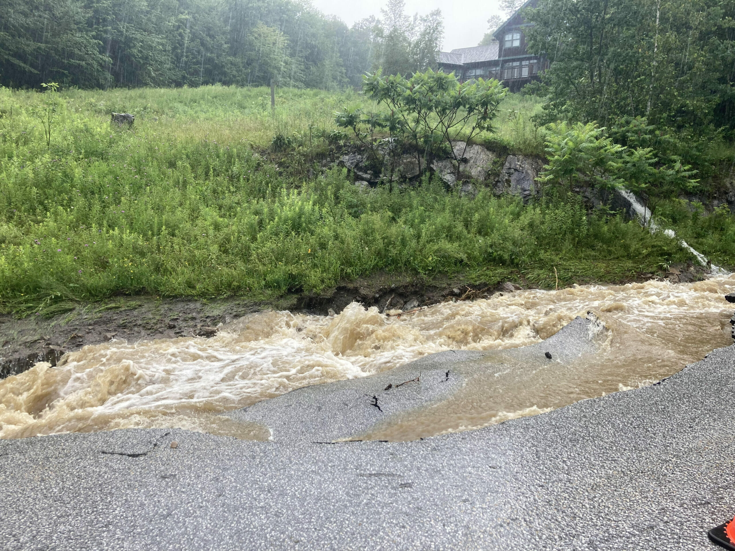 Rain water floods the side of a road, destroying the pavement