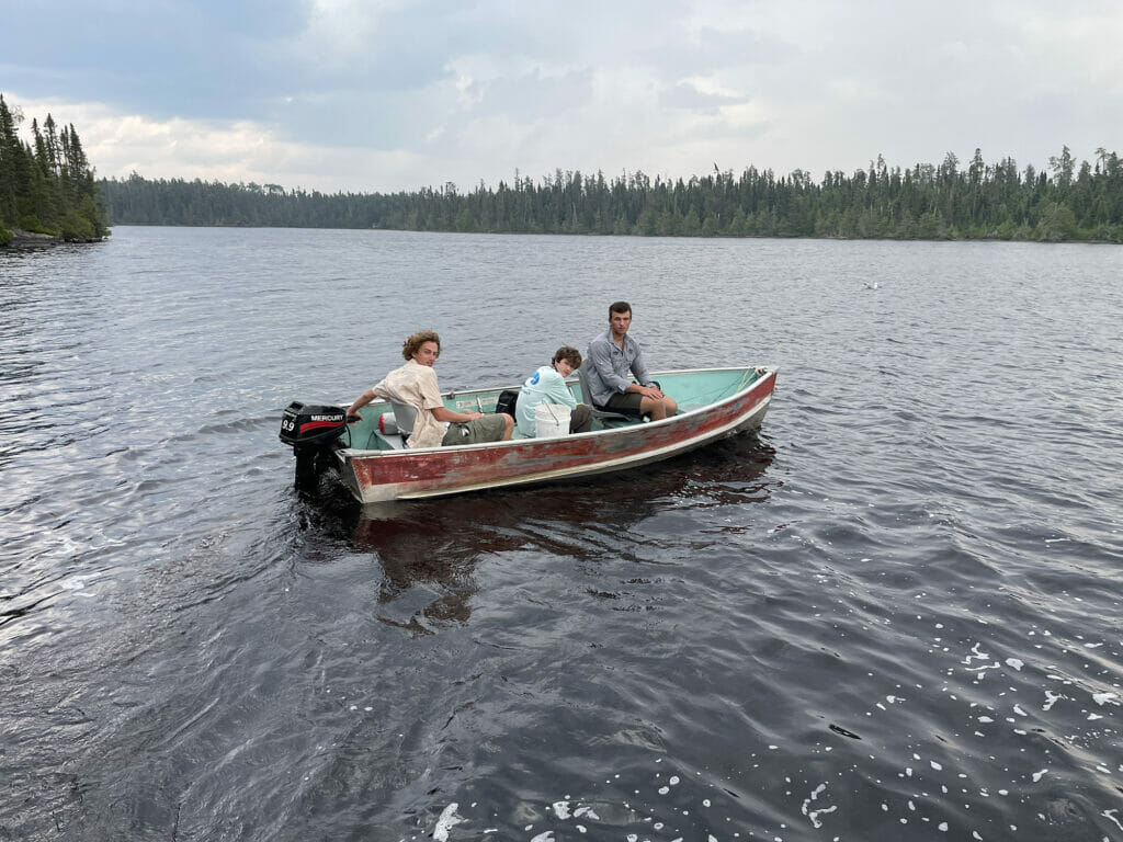 Three young men in a beat-up motor boat on a beautiful lake