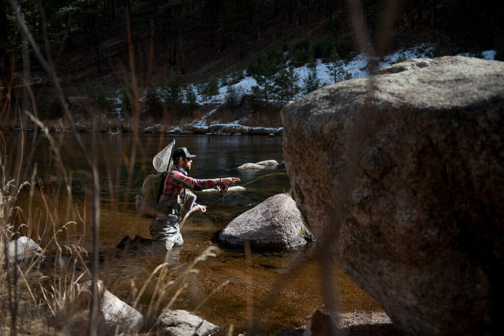 man's backcast helps his cast in a river with large rocks