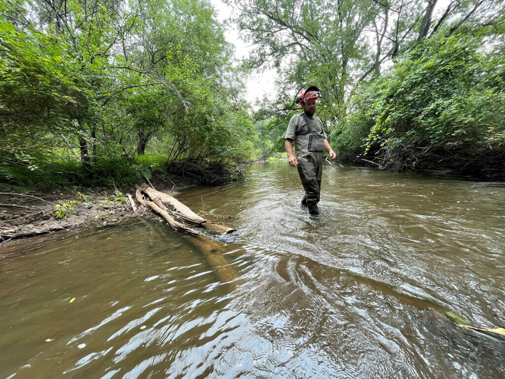 Man in waders walks thought stream