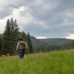 Man with a fishing pole walks through a glen towards mountains