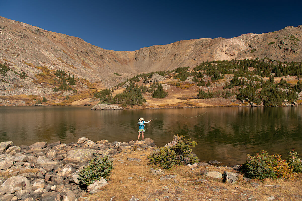 Woman casts into a large lake with rocky hills behind it