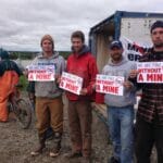 Four men stand with signs reading "We are fine without a mine. No Pebble Mine"
