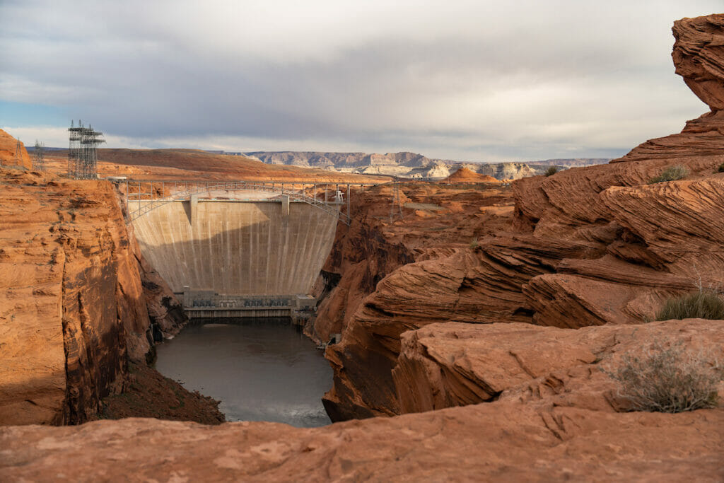A dam surrounded by dried red rocks and mountains in the background