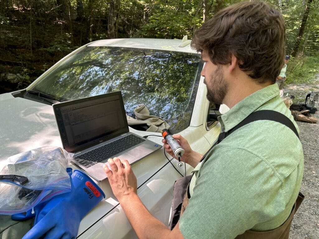 Man in the woods with laptop and equipment on hood of a truck