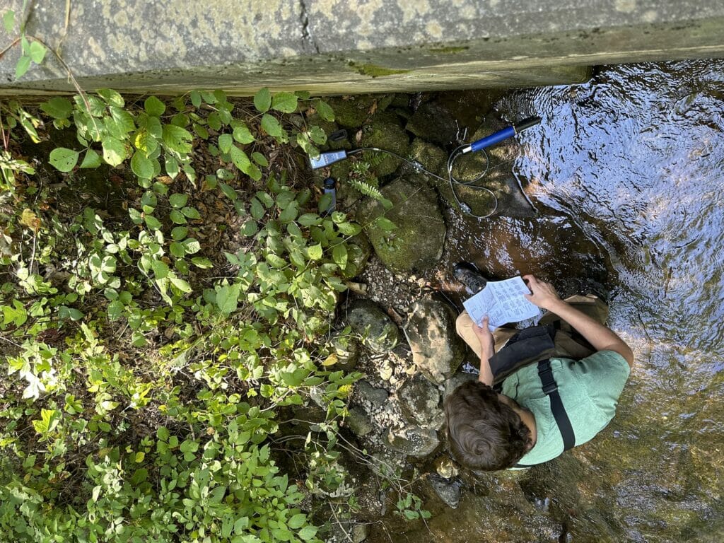 View from above of man in a stream with notebook and equipment