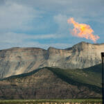 Flames come out of a pipe in front of beautiful mountains