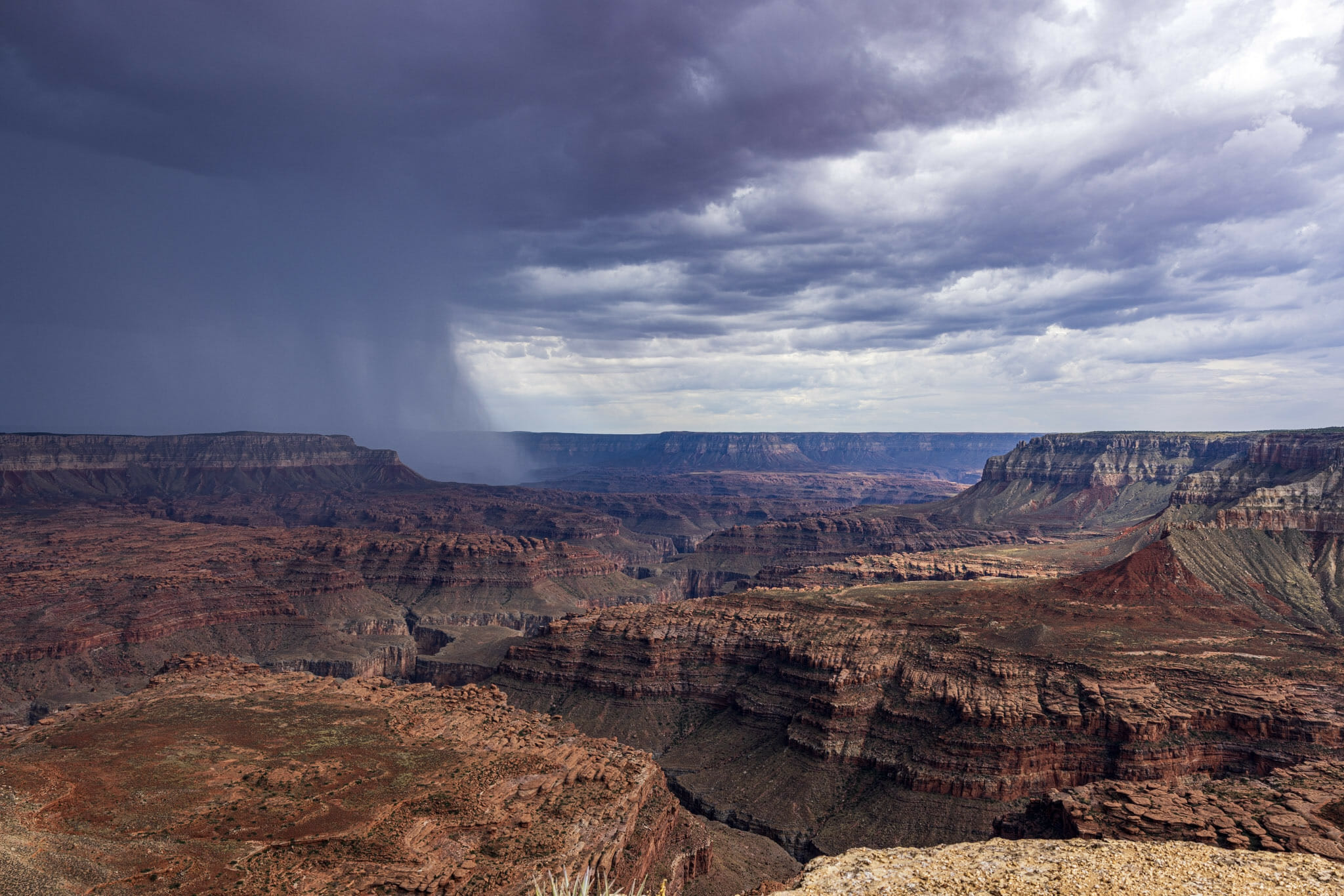 A wide view Multi-colored levels of the Grand Canyon with rain coming in from the left