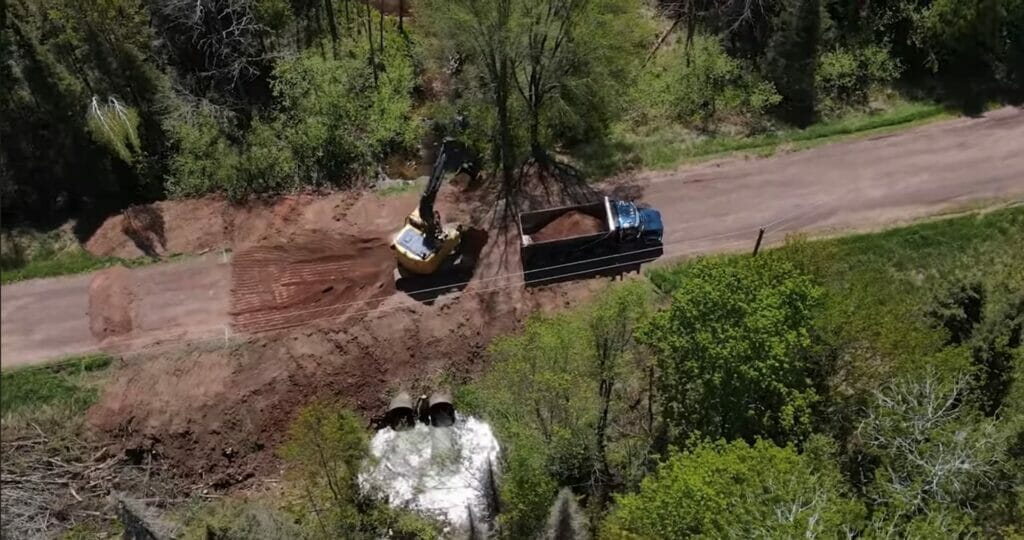 Truck and backhoe lifting dirt next to two culverts helping Trout Infrastructure