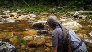 A man casts into a small stream with many stones