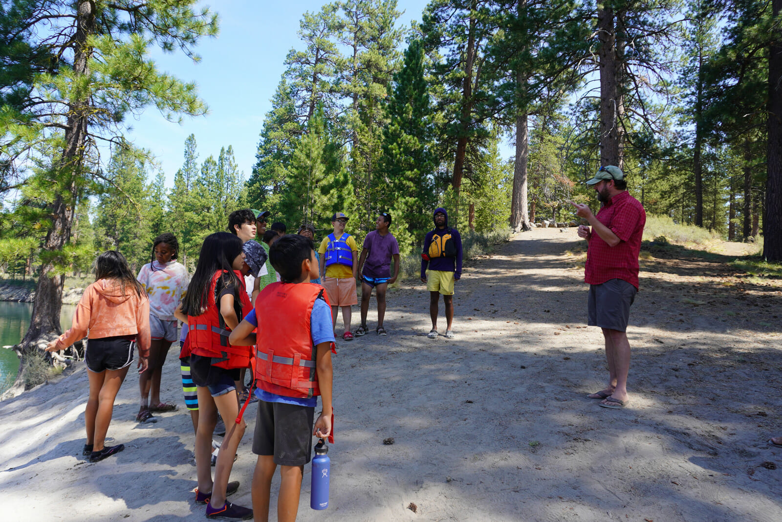 Man talks to a group of kids wearing life preservers by a river