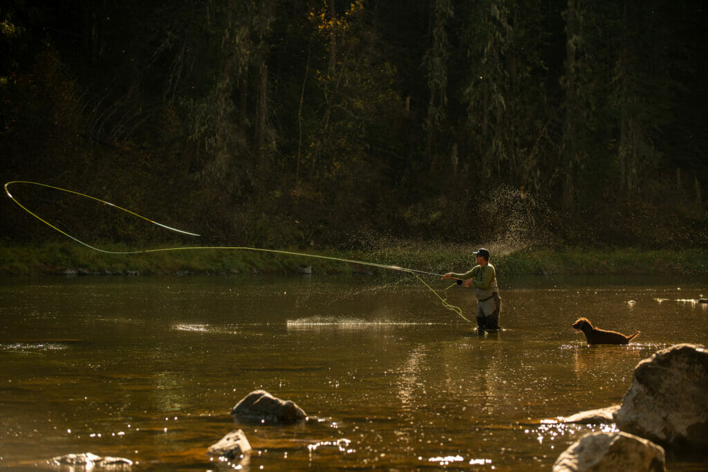 Man casting a fly while his dog watching who is happy to be there