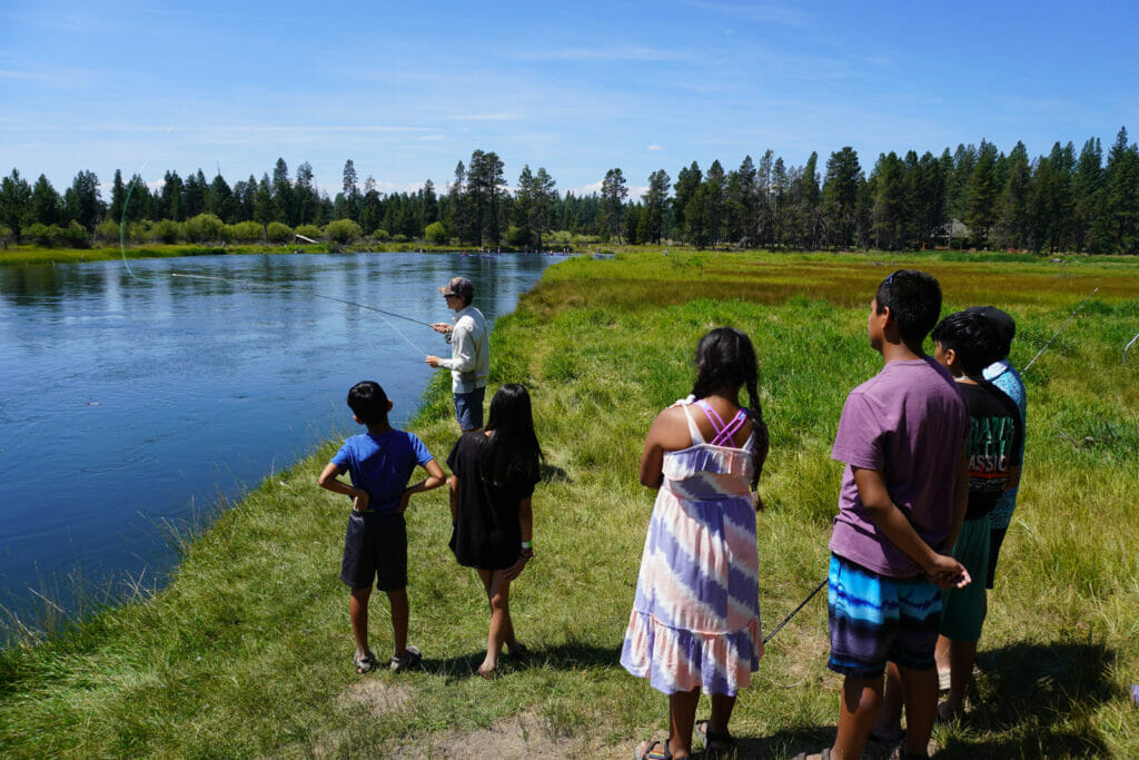 Man fishes while several Latinx children watch
