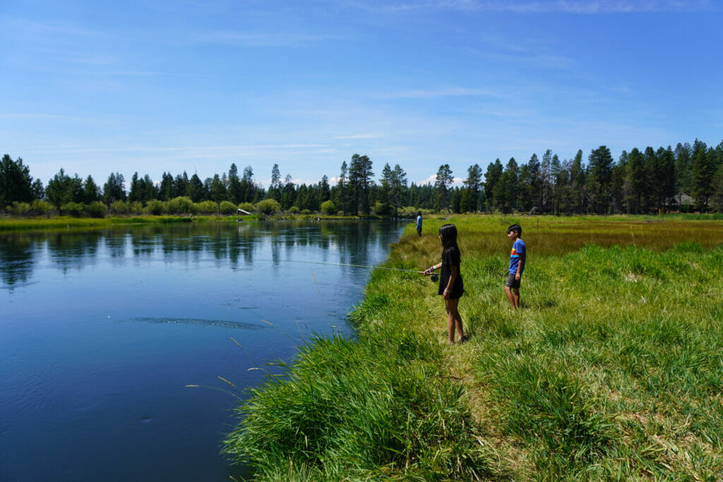 A child fishes in a river while another child watches