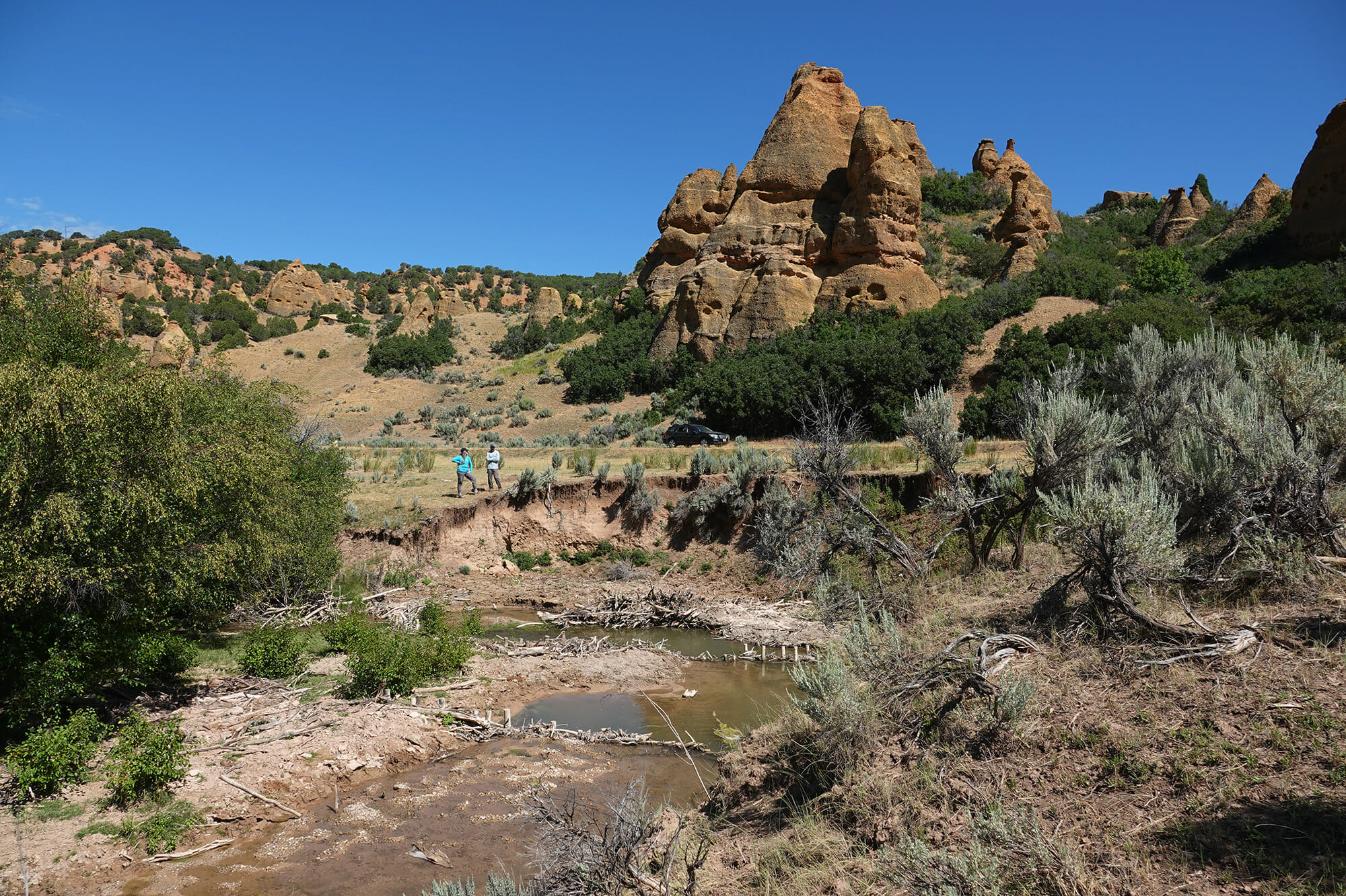 Two people stand next to some water by some big rocks