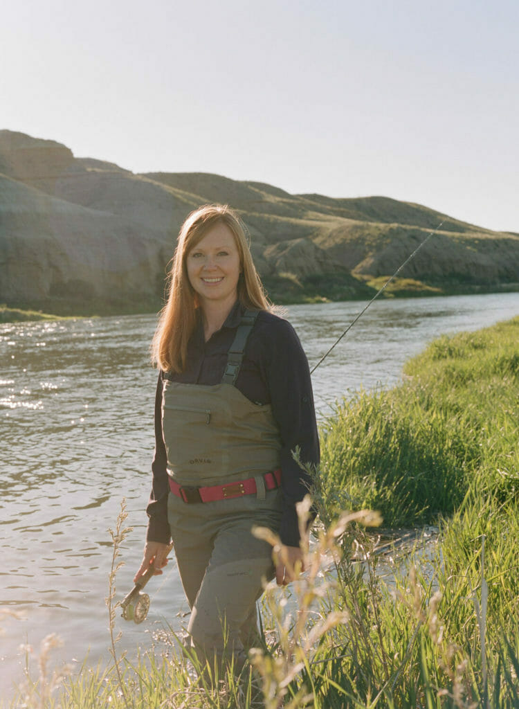 Woman in waders walking in river with a fishing pole working towards restoration