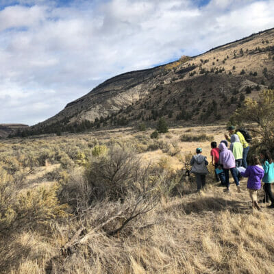 A teacher and seven 3rd graders walk through a dry landscape next to a mountain