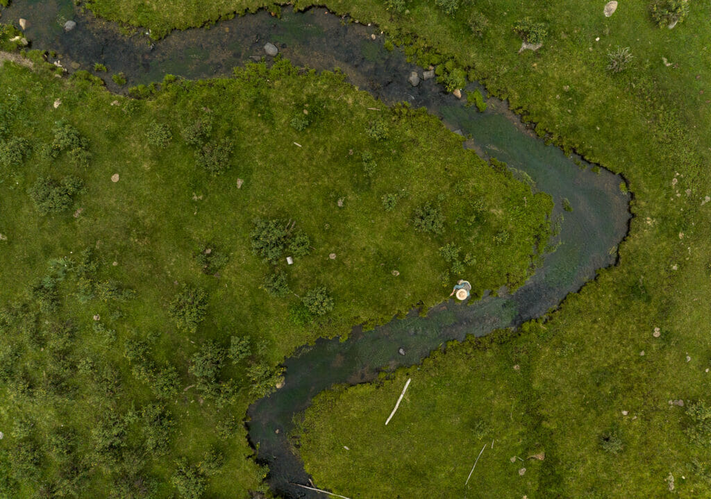 Areal view of someone with a hat fishing in a winding stream