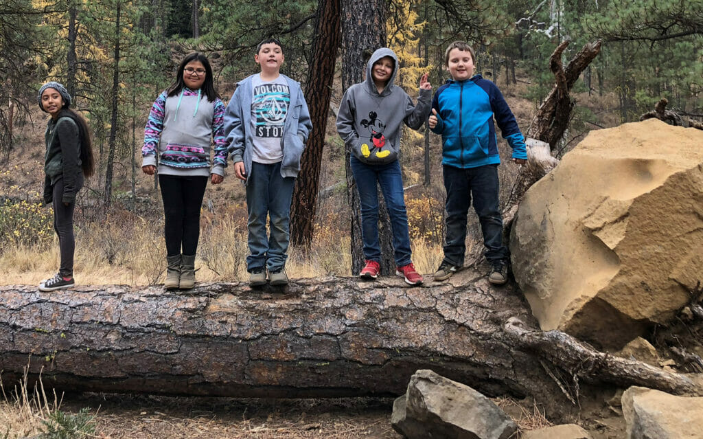 Five 4th graders stand on a fallen tree posing for the photo