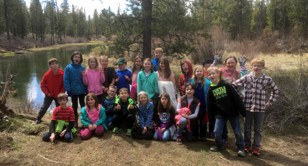 Two dozen smiling elementary students pose next to a river