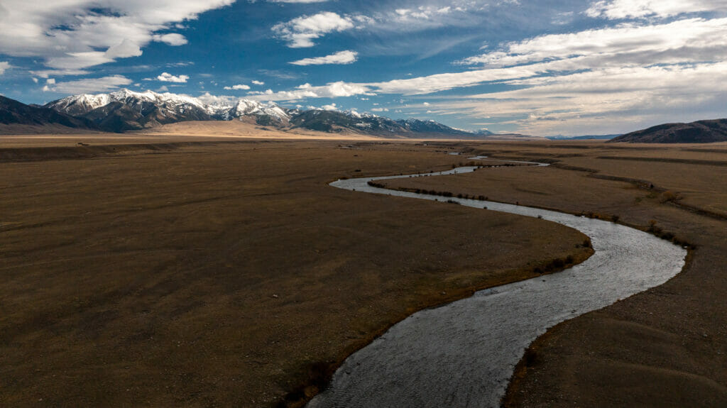 A winding stream on a plain with snow capped mountains in the background