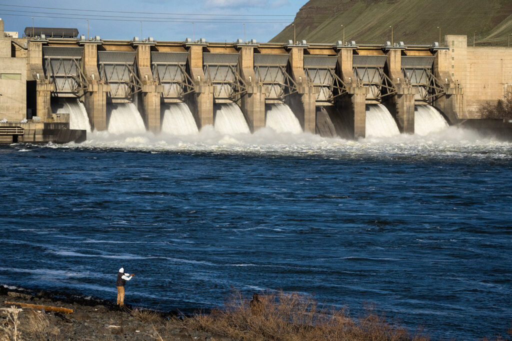 person fishing near monumental dam on snake river while floodgates are open