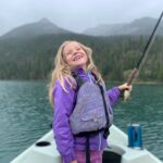 young girl in a boat holding a fly rod with a big smile
