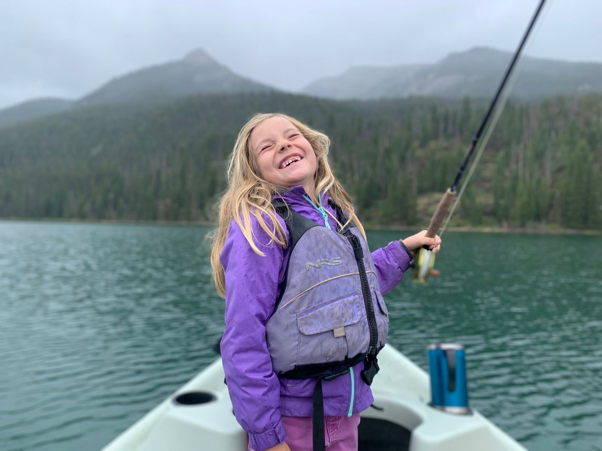young girl in a boat holding a fly rod with a big smile